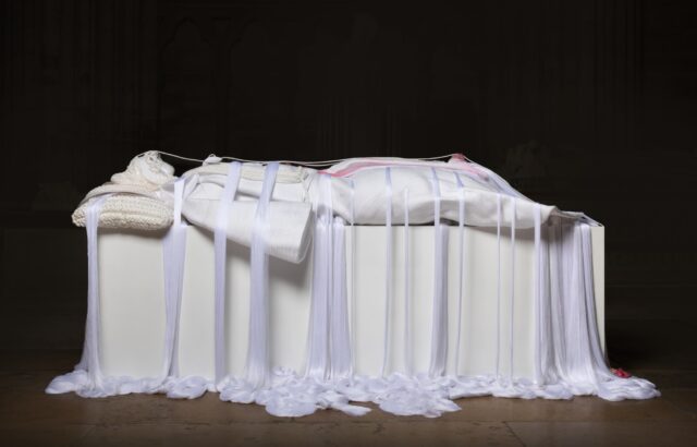 a mixed media white rope sculpture of a female figure laying down, referencing noble sculptures on top of sarcophagi, with draping ropes pooling at the floor